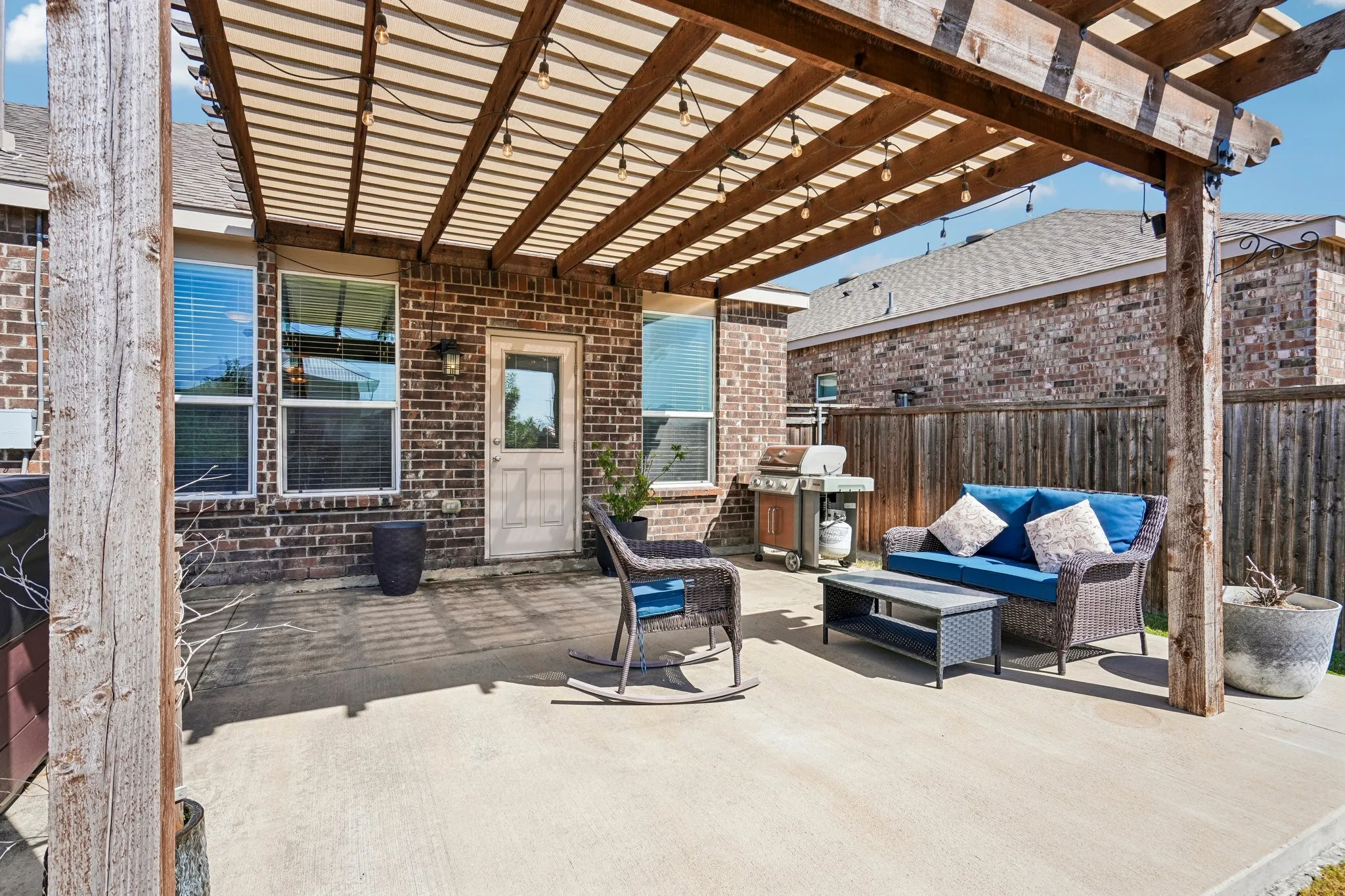 Concrete patio featuring a wood pergola with string lighting, brick exterior, and a privacy fence