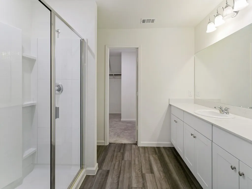 Glass-enclosed shower with built-in shelving, extensive vanity with integrated sink, white cabinetry, and wood-finish flooring