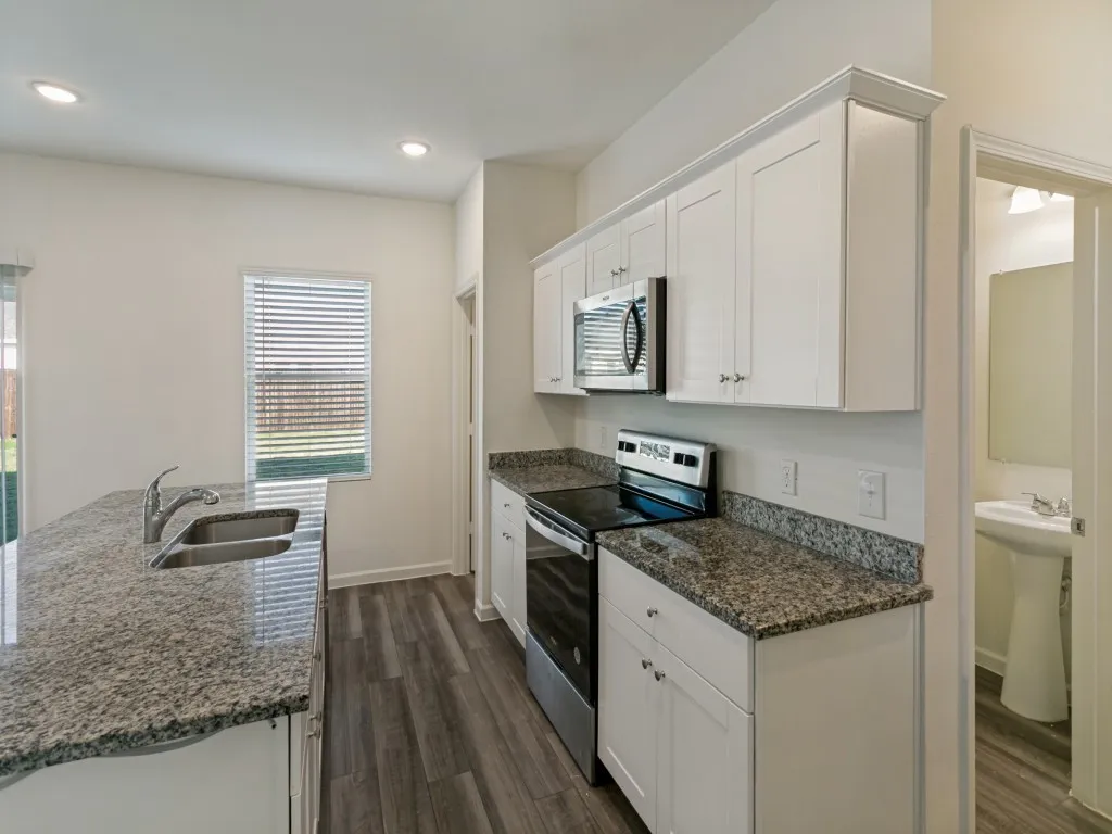 Kitchen featuring wood-finish flooring, white cabinetry, granite countertops, stainless steel appliances, and a built-in sink