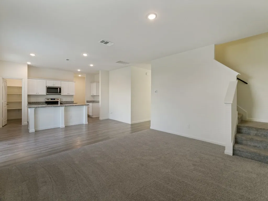 Open-concept living area featuring wood-finish flooring, recessed lighting, and a kitchen with white cabinetry, stainless steel appliances, and a breakfast bar