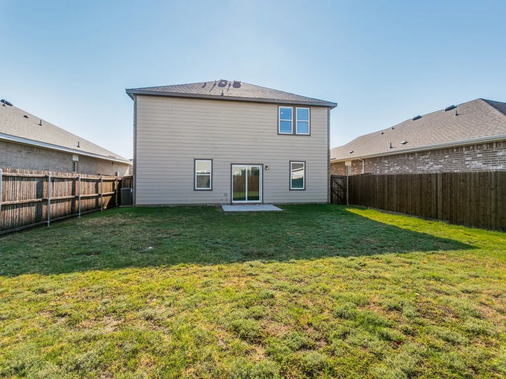 Expansive backyard with a manicured lawn, full privacy fencing, and a concrete patio