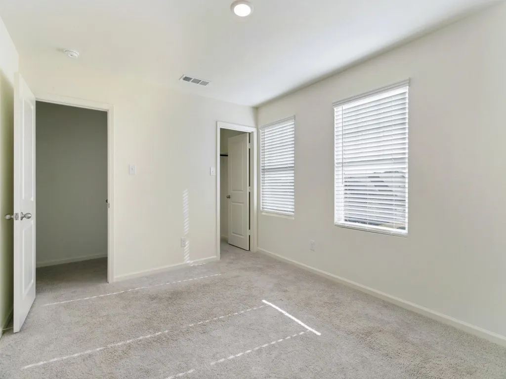 Neutral tone wall paint, light gray carpet flooring, two windows with blinds, and white interior doors