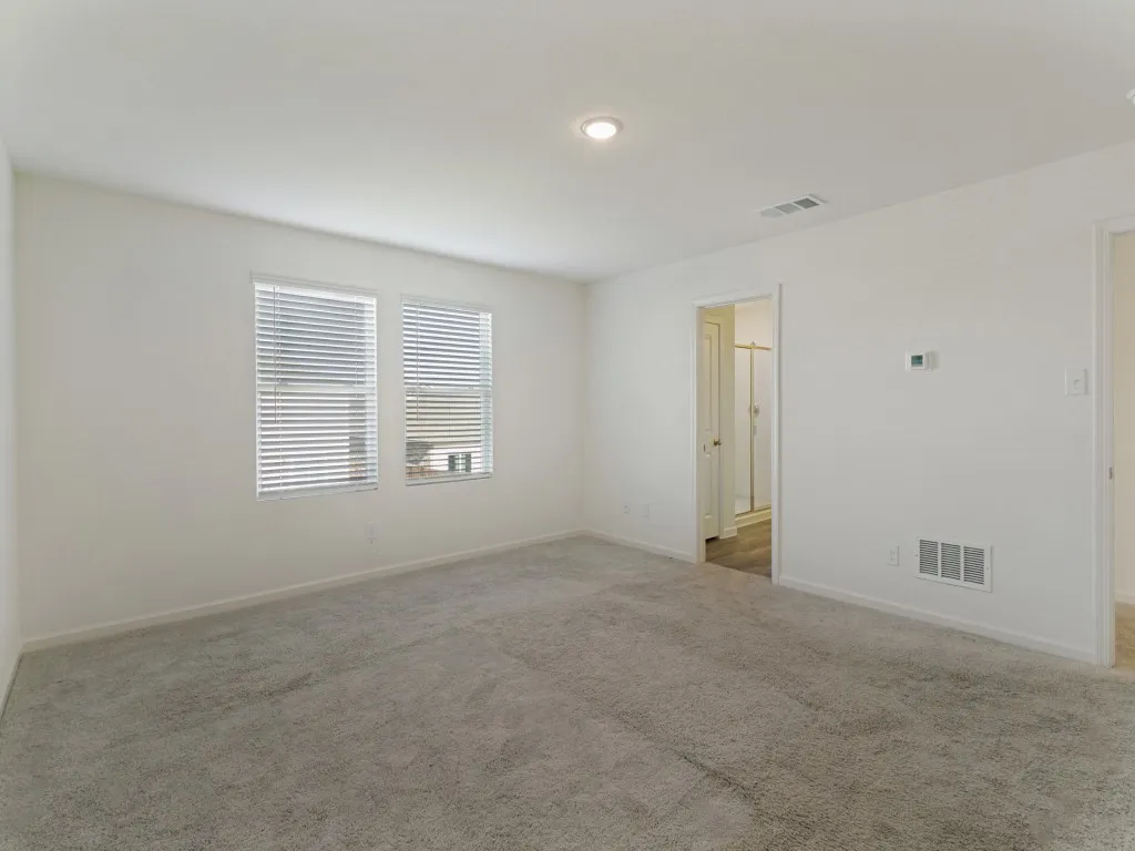 Soft gray carpeting throughout, recessed ceiling lighting, and two windows with blinds