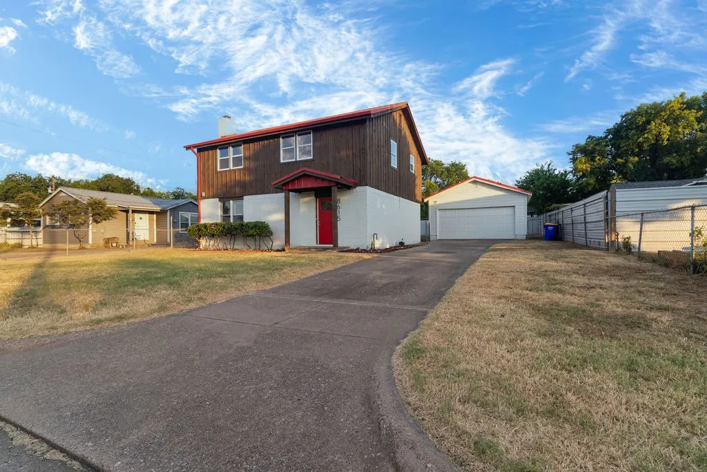 Two-story residence with a red door, an attached single-car garage, a paved driveway, and a chain-link fence