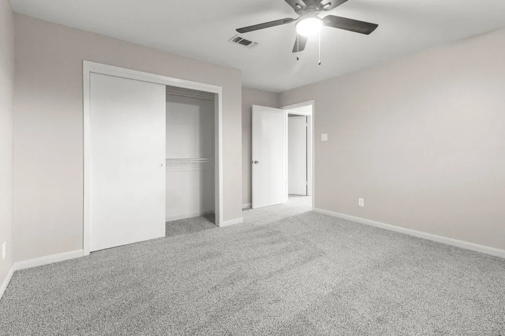 Neutral wall tones, gray carpeting, sliding closet doors, and a ceiling fan with integrated lighting