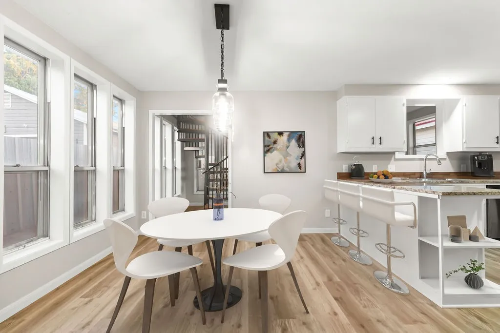 Bright dining area with wood-finish flooring, multiple windows, and a modern pendant light fixture