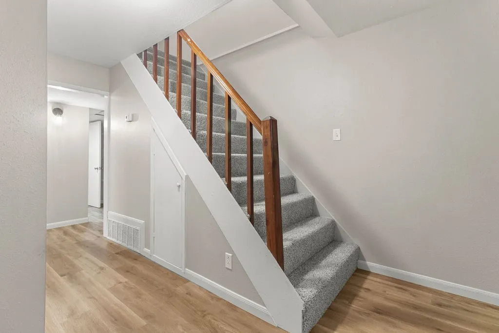 Wood-finish flooring, light grey walls, carpeted staircase, and wood handrail