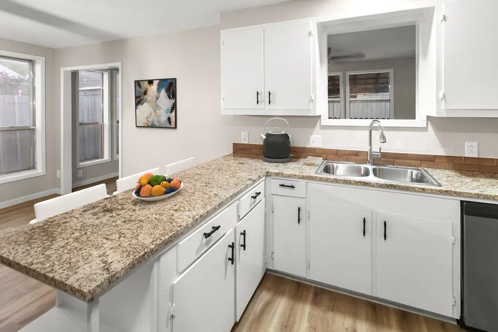 Kitchen featuring white cabinetry, a dual basin sink, wood-finish flooring, and light-colored countertops