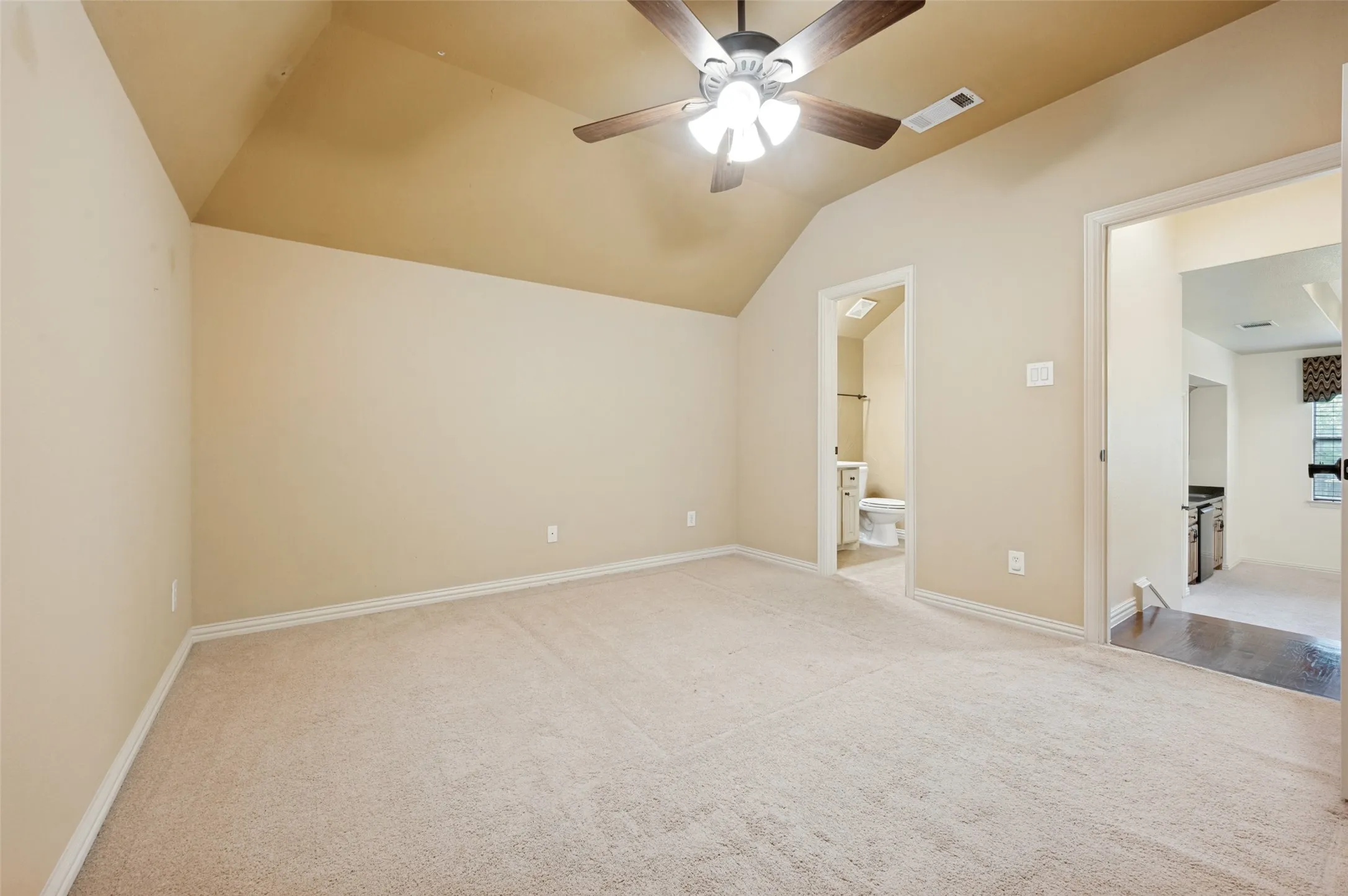 Vaulted ceiling with an integrated ceiling fan, light-colored carpeting, and a neutral wall palette