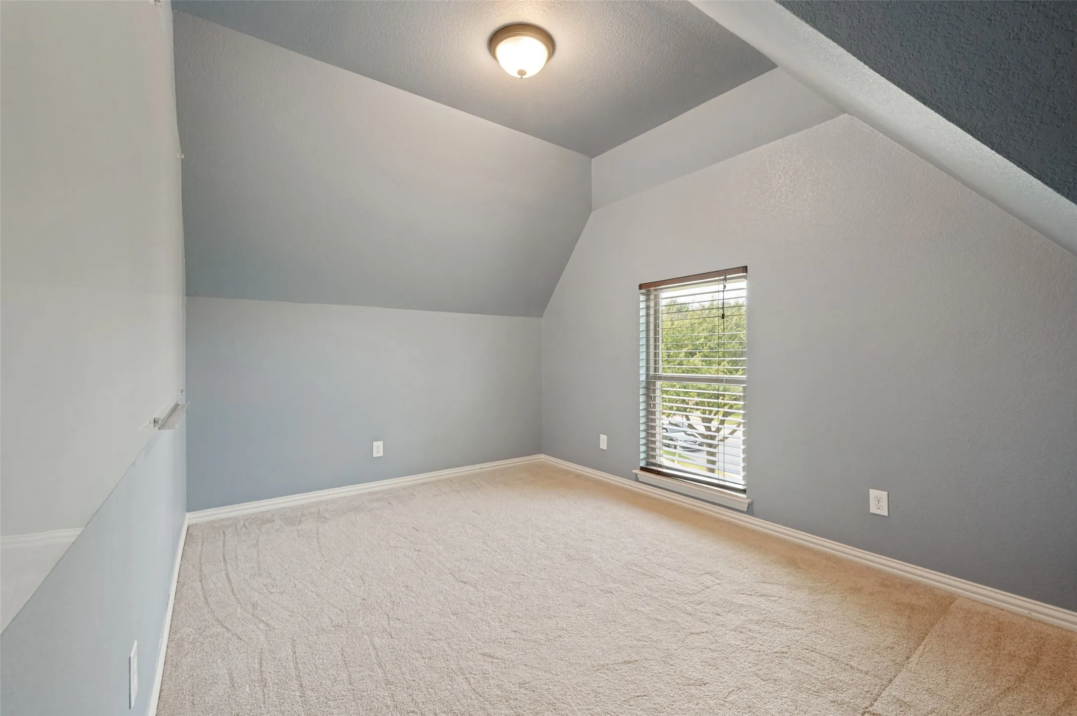 Attic room with sloped ceilings, a single window with blinds, and light-colored carpeting