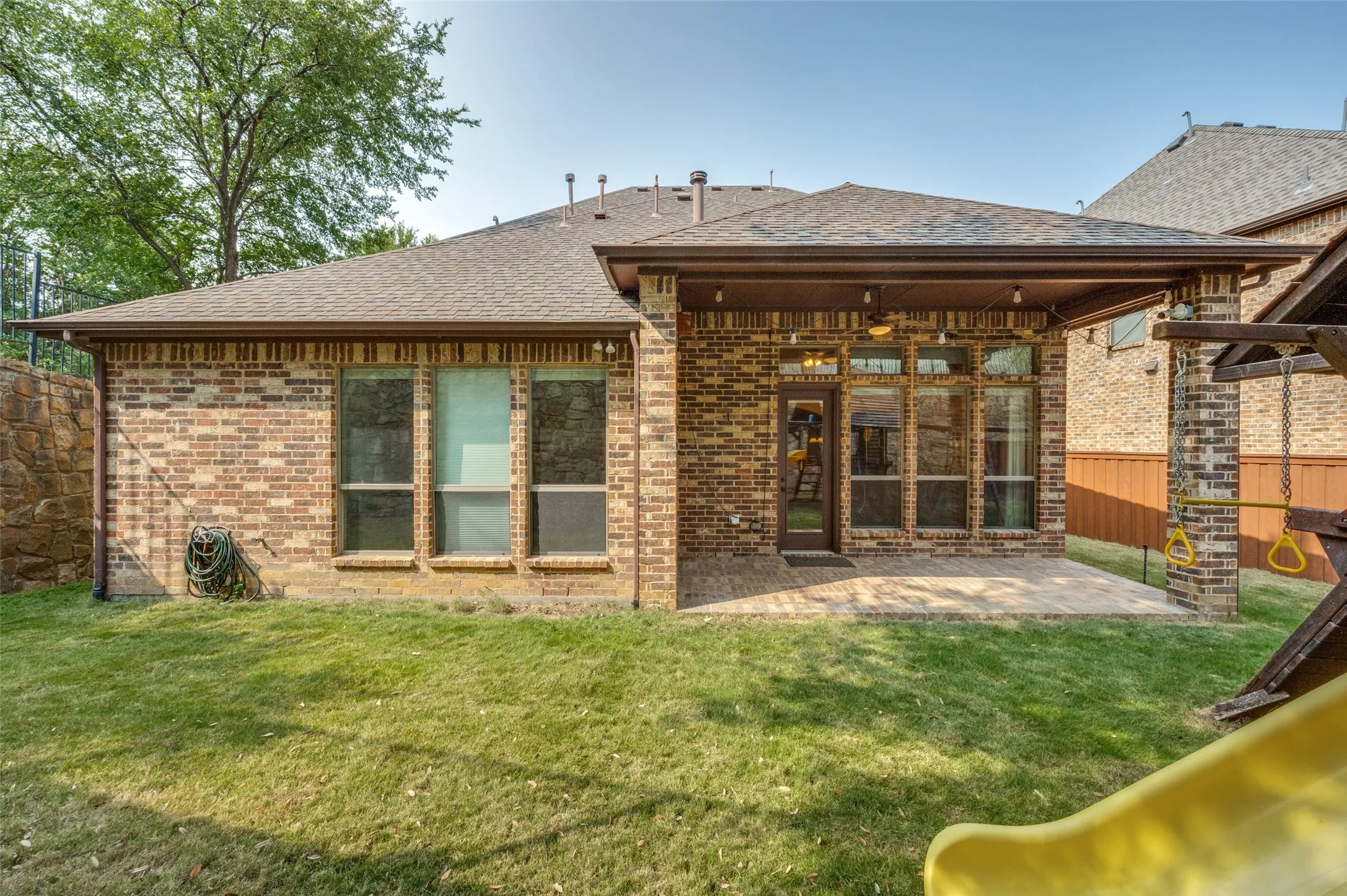 Brick exterior featuring a covered patio with recessed lighting and a ceiling fan, a flagstone retaining wall, and a manicured lawn