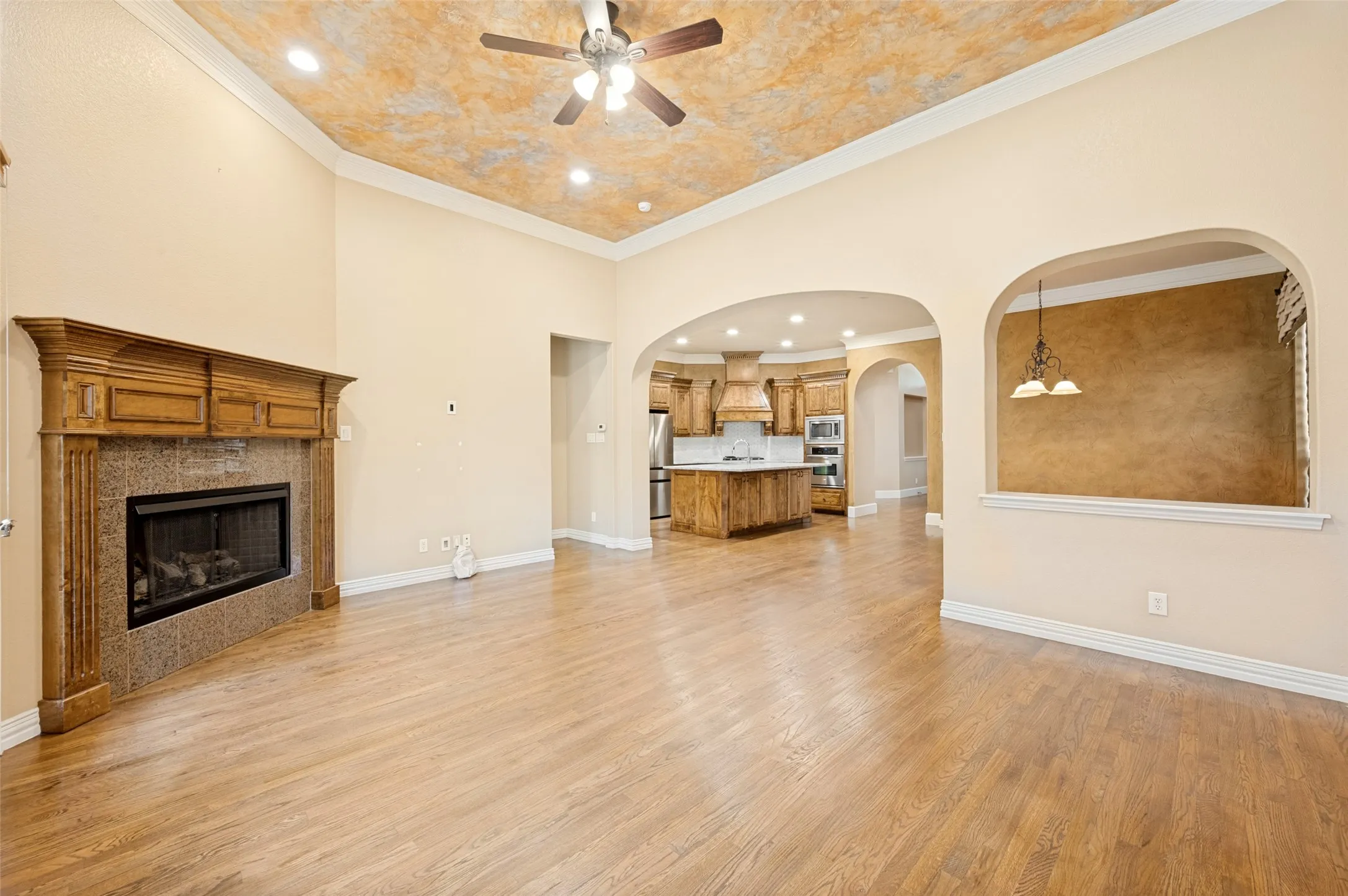 Wood-finish flooring throughout, a fireplace with a stone surround and wood mantel, decorative archways, a ceiling fan, and recessed lighting