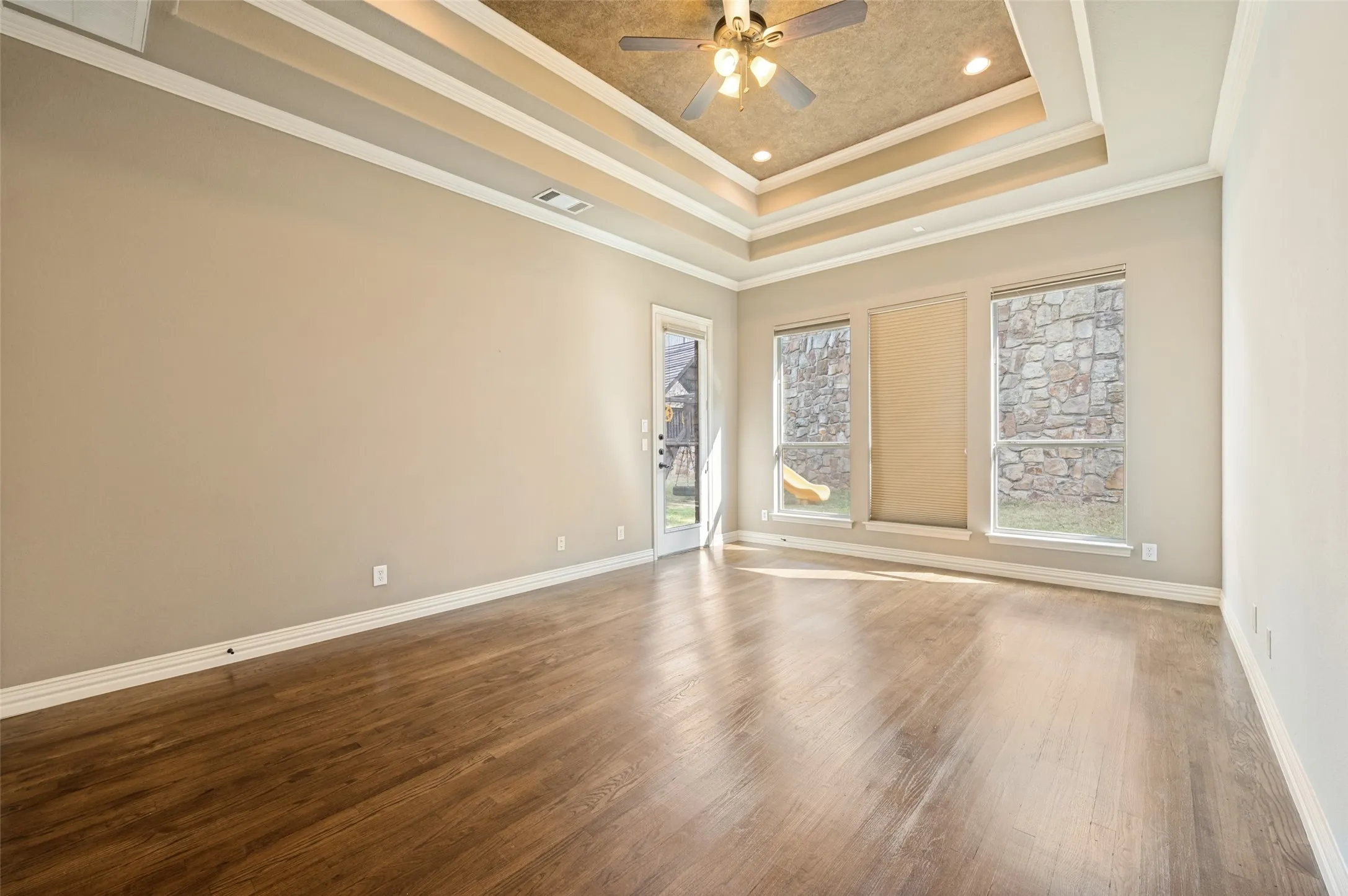 Tray ceiling with crown molding, wood-finish flooring, recessed lighting, ceiling fan, and multiple windows