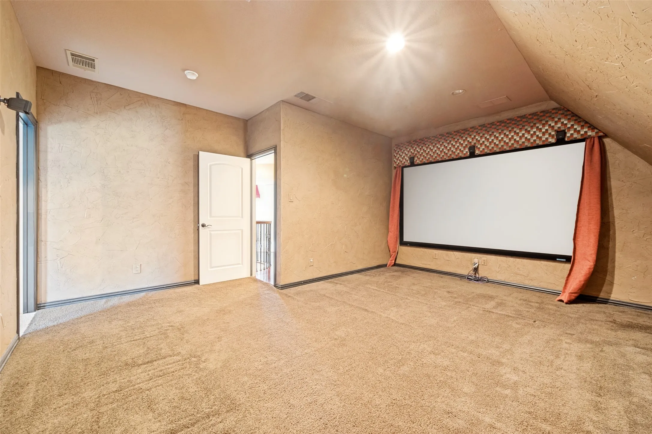 Carpeted room featuring an integrated projection screen, an angled ceiling, and a paneled white door