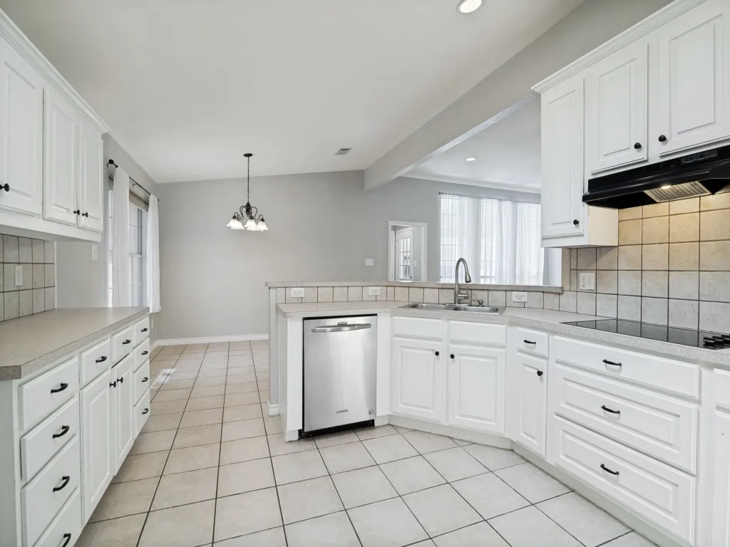 White cabinetry with dark hardware, stainless steel dishwasher, tile backsplash, tile flooring, and pendant lighting
