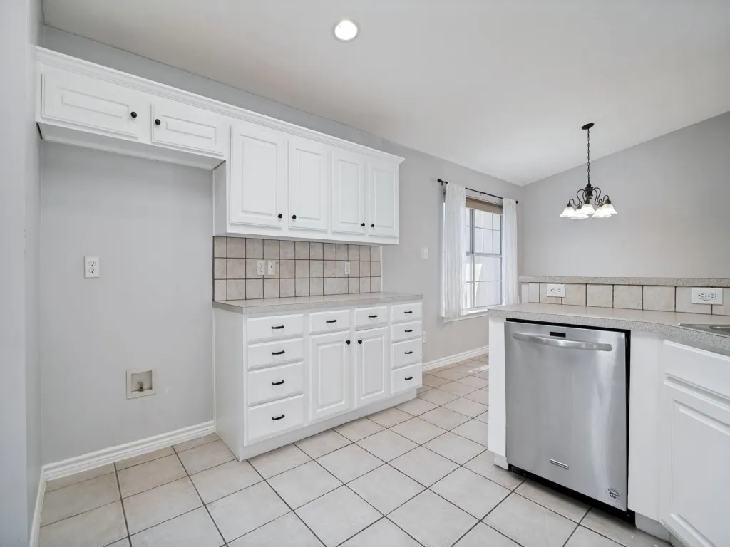 White cabinetry with black hardware, tile flooring, light-toned countertops, tile backsplash, and a stainless steel dishwasher