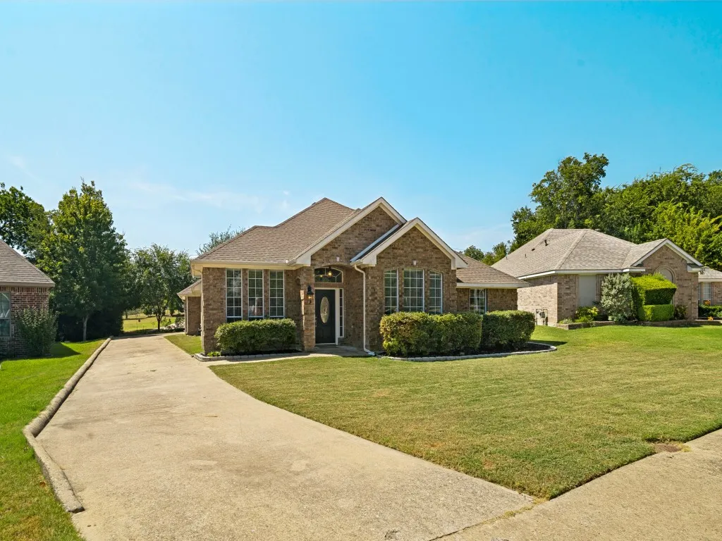 Brick exterior with a gabled roofline, mature landscaping, and an arched entry door