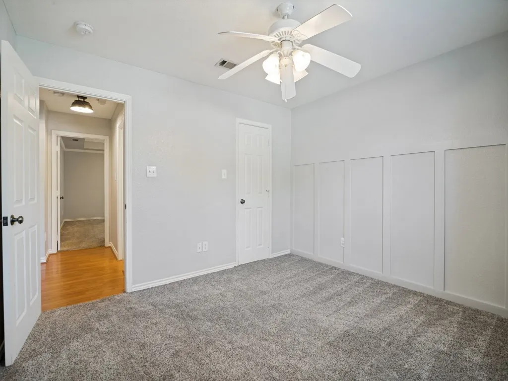 Wall paneling detail, ceiling fan with integrated lighting, neutral-toned carpet, white interior door, and light gray wall paint