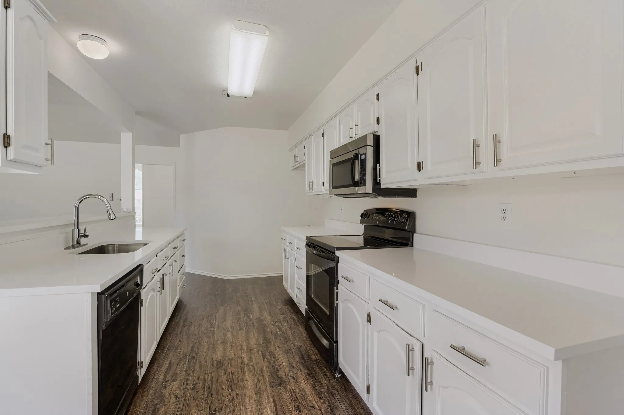 Kitchen featuring white cabinetry, white countertops, stainless steel sink, black dishwasher, and black range with microwave