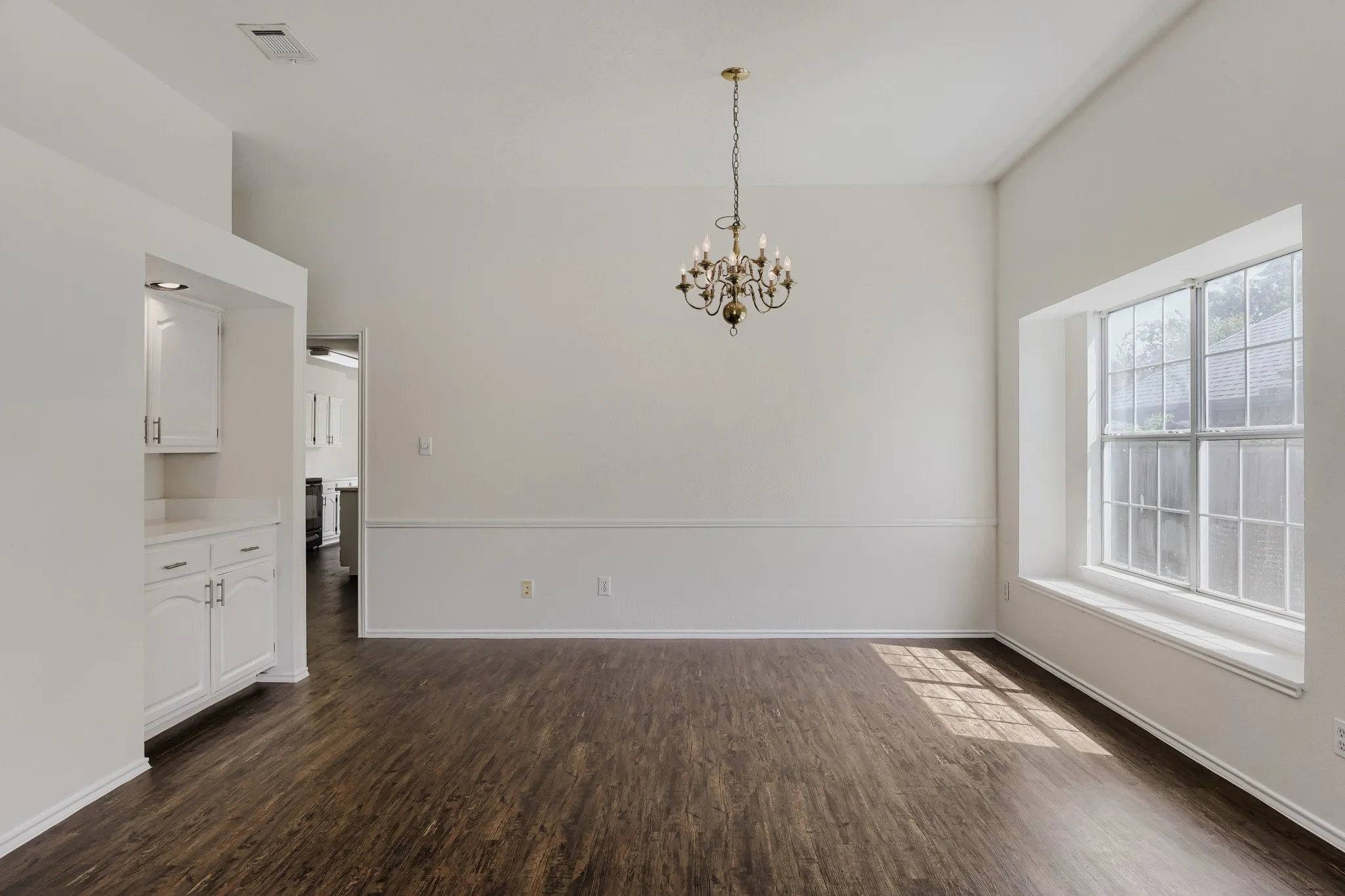 Vaulted ceiling with an ornate chandelier, wood-finish flooring, built-in cabinetry, and a large window with a deep sill