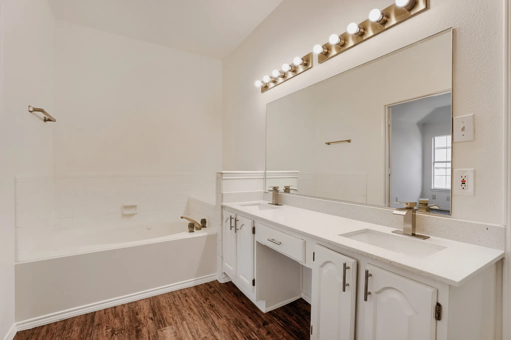 Spa-inspired primary bathroom featuring dual vanities with white cabinetry, white quartz countertops, polished nickel fixtures, and an illuminated mirror