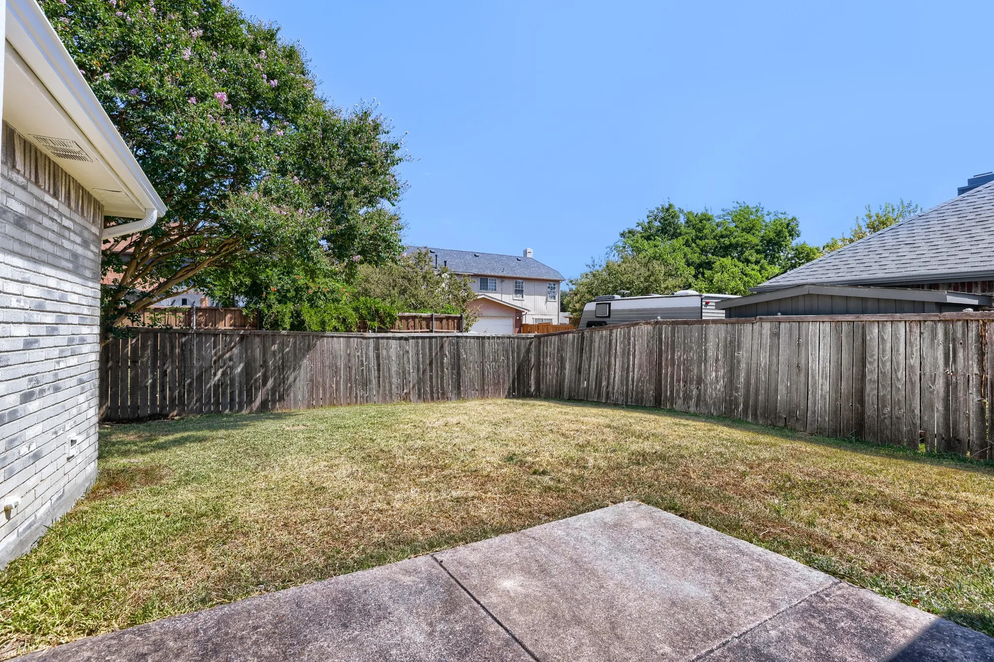 Expansive backyard with a concrete patio, wood privacy fencing, and mature trees