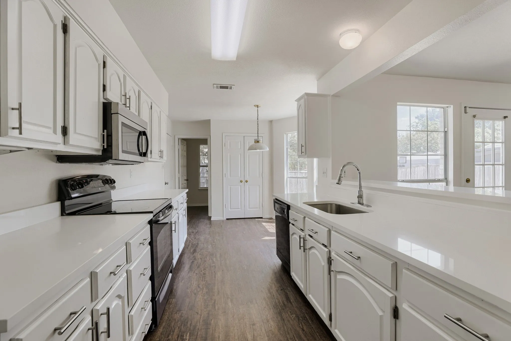 Kitchen featuring white cabinetry, white countertops, a stainless steel sink, wood-finish flooring, and a stainless steel microwave