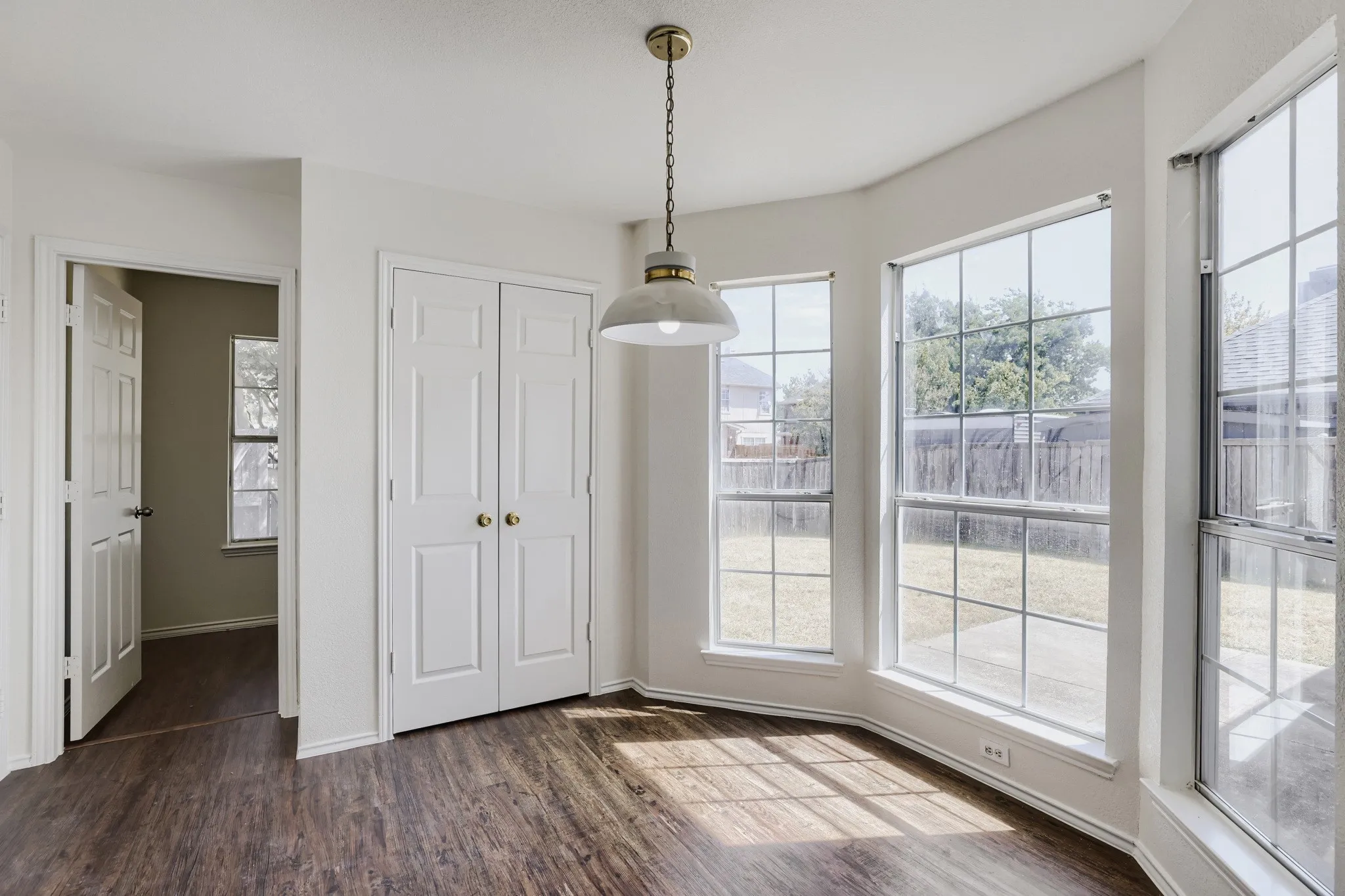 Bay window with multiple glass panes, wood-finish flooring, white bifold doors, and a decorative pendant light fixture