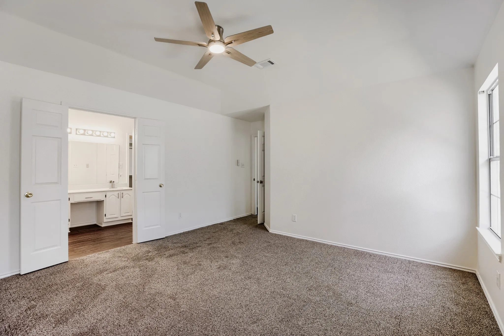 Spacious room with plush carpeting, natural light from a double-pane window, and a ceiling fan with integrated lighting
