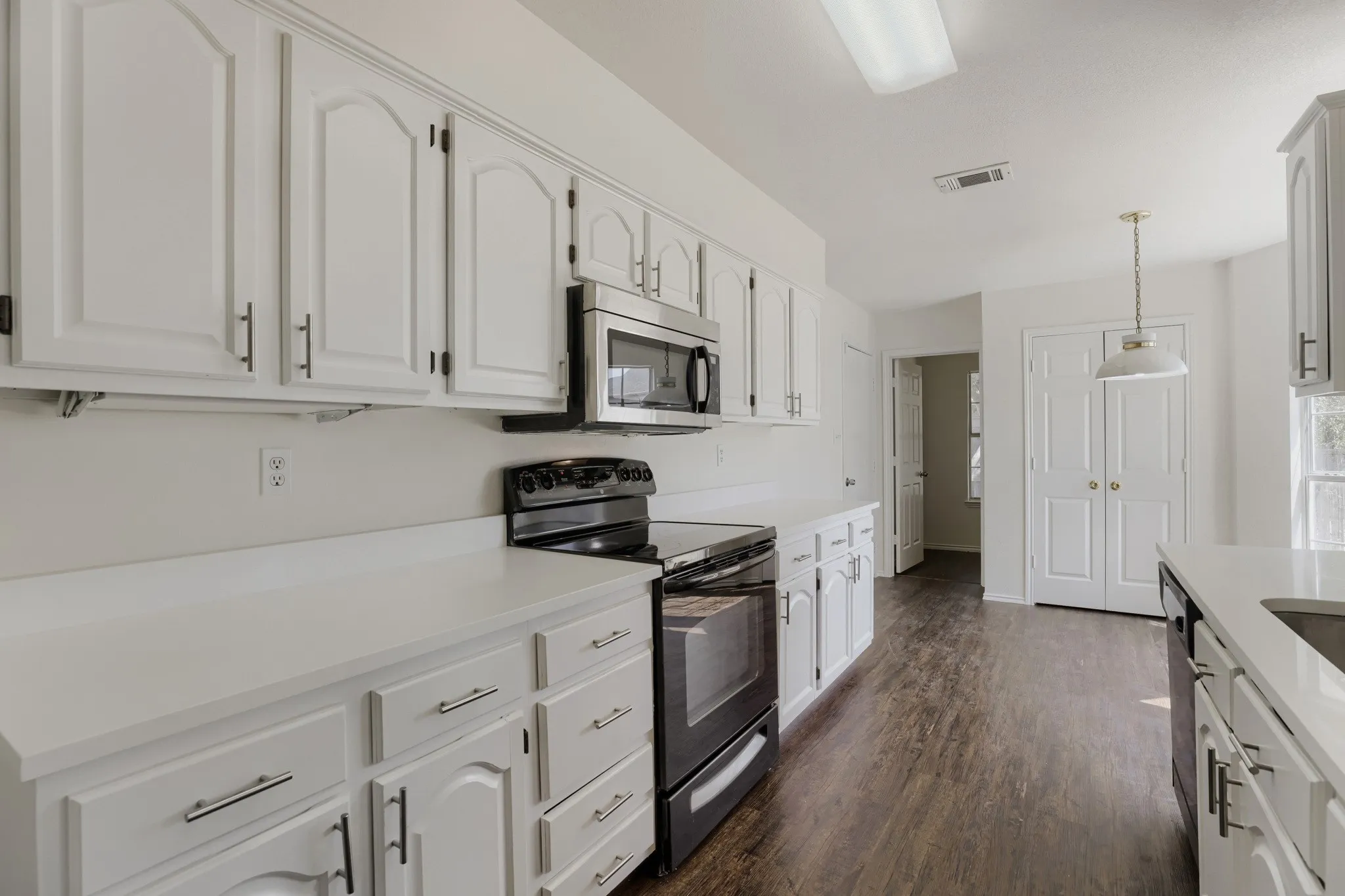 Kitchen featuring white cabinetry, light-colored countertops, wood-finish flooring, a stainless steel microwave, and a black range