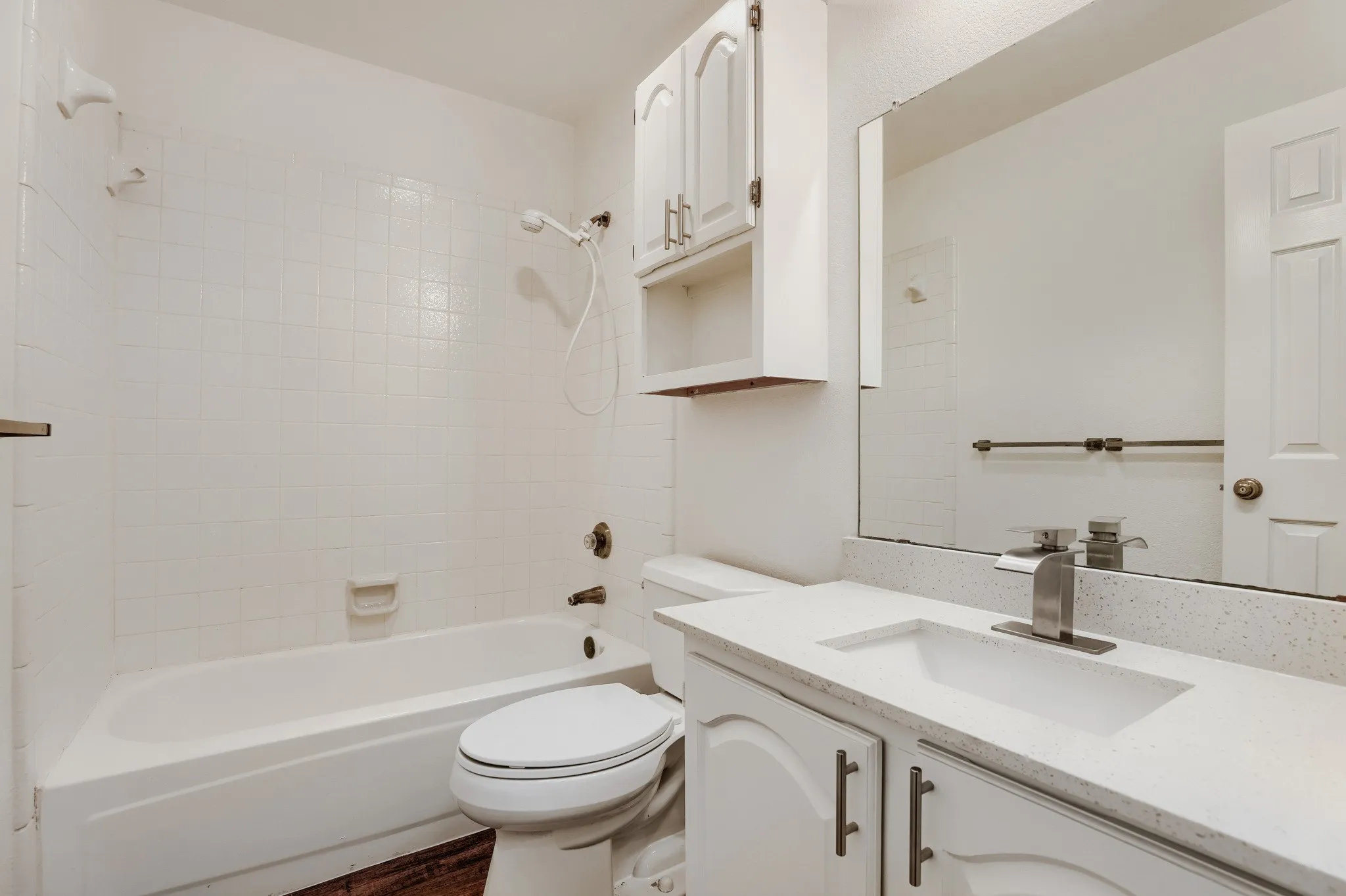 Clean, modern bathroom featuring a white subway tile shower surround with glass enclosure, white vanity with dual sink basin and brushed nickel hardware, large mirror with integrated lighting, and white porcelain toilet