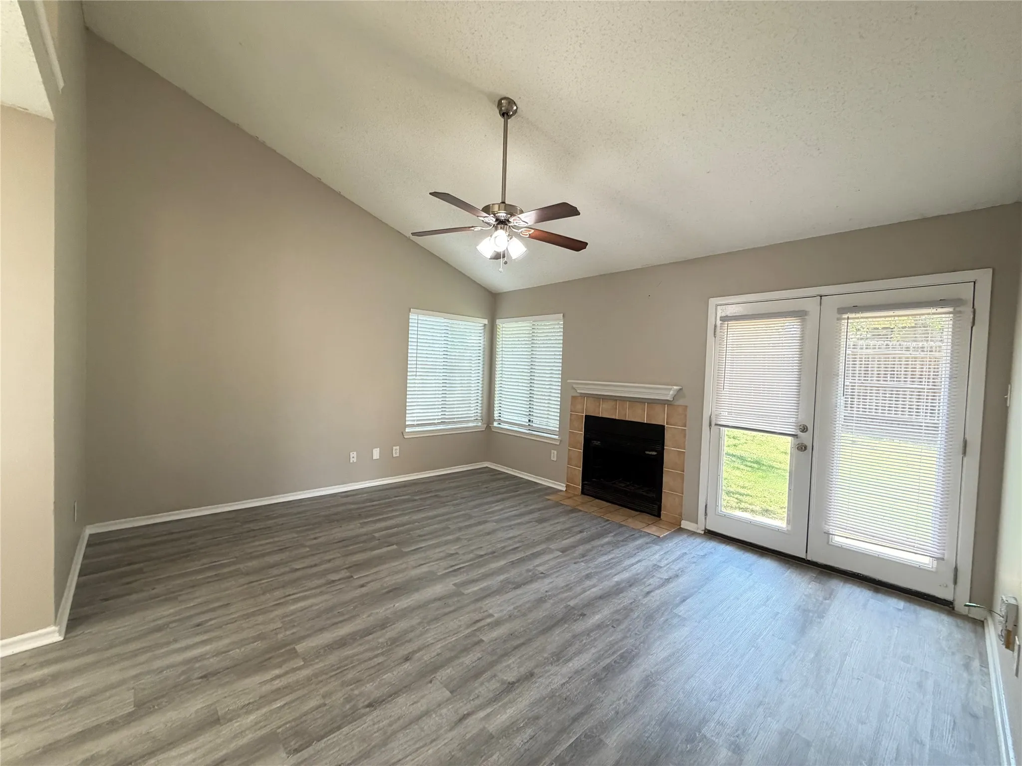 Vaulted ceiling with ceiling fan, wood-finish flooring, brick fireplace surround with mantel, and double French doors to the exterior