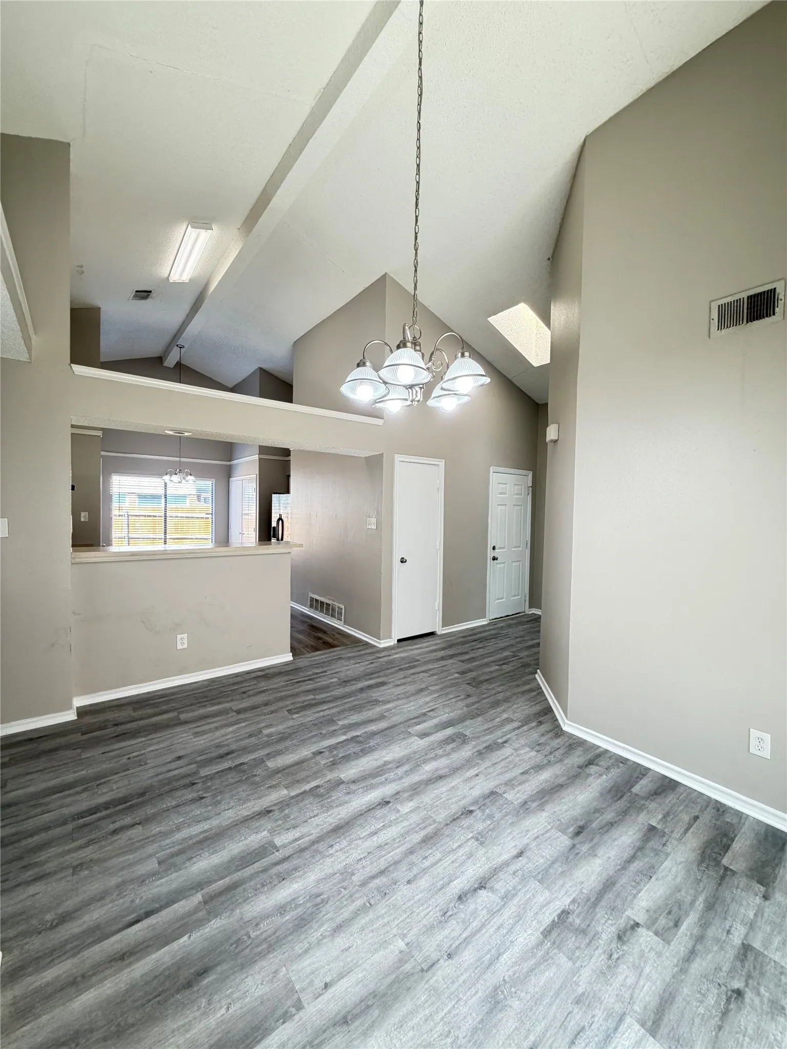 Vaulted ceilings, wood-finish flooring, skylight, and a contemporary chandelier