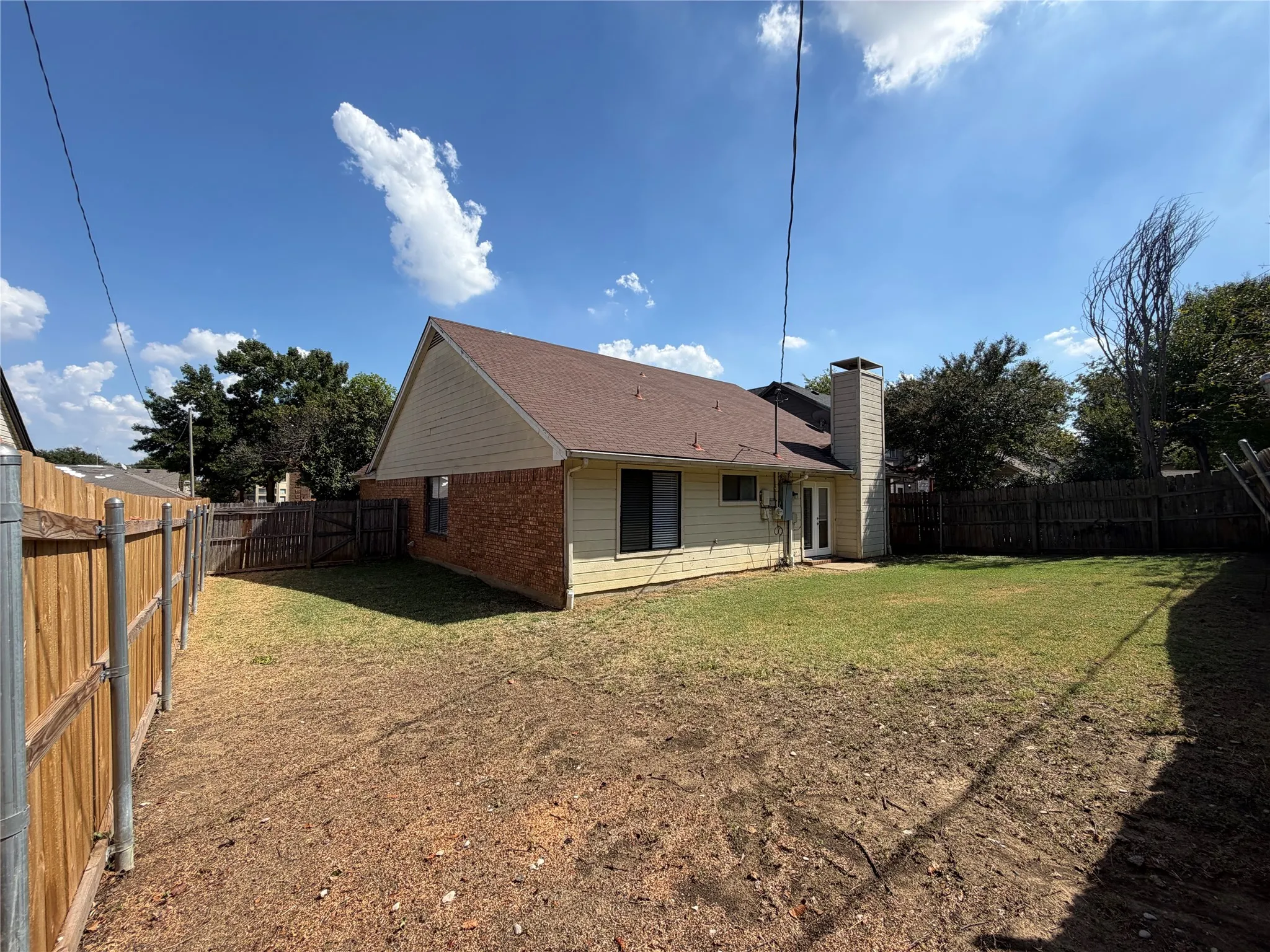 Fenced backyard featuring a brick and siding exterior, a prominent chimney, and a rear entry door