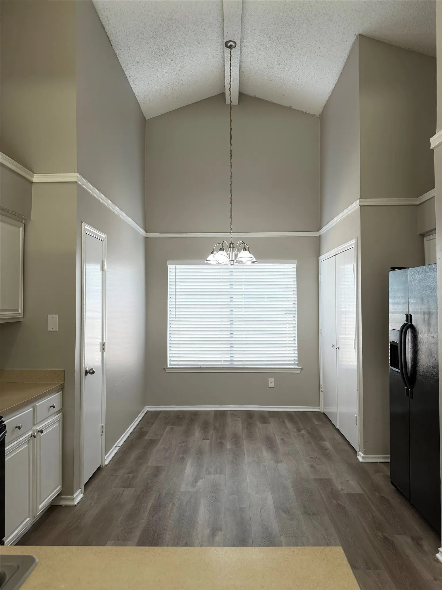 Vaulted ceiling, wood-finish flooring, white window blinds, built-in cabinetry, and a black refrigerator