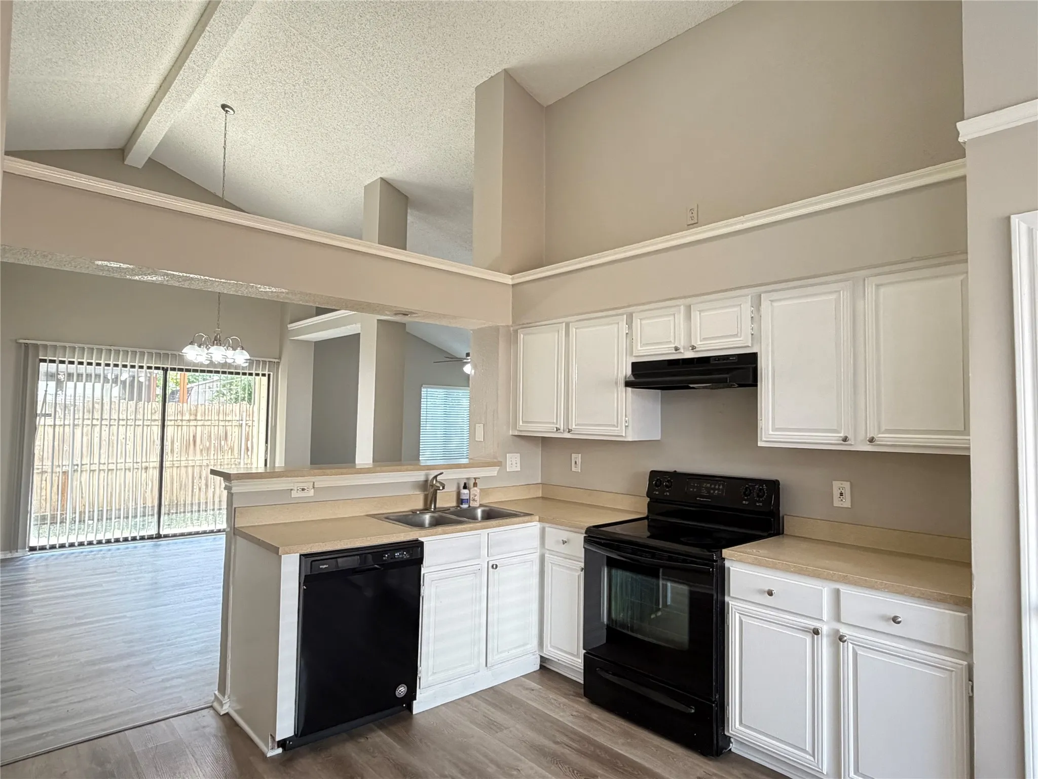 Kitchen featuring white cabinetry with dark hardware, black appliances, wood-finish flooring, and a vaulted ceiling