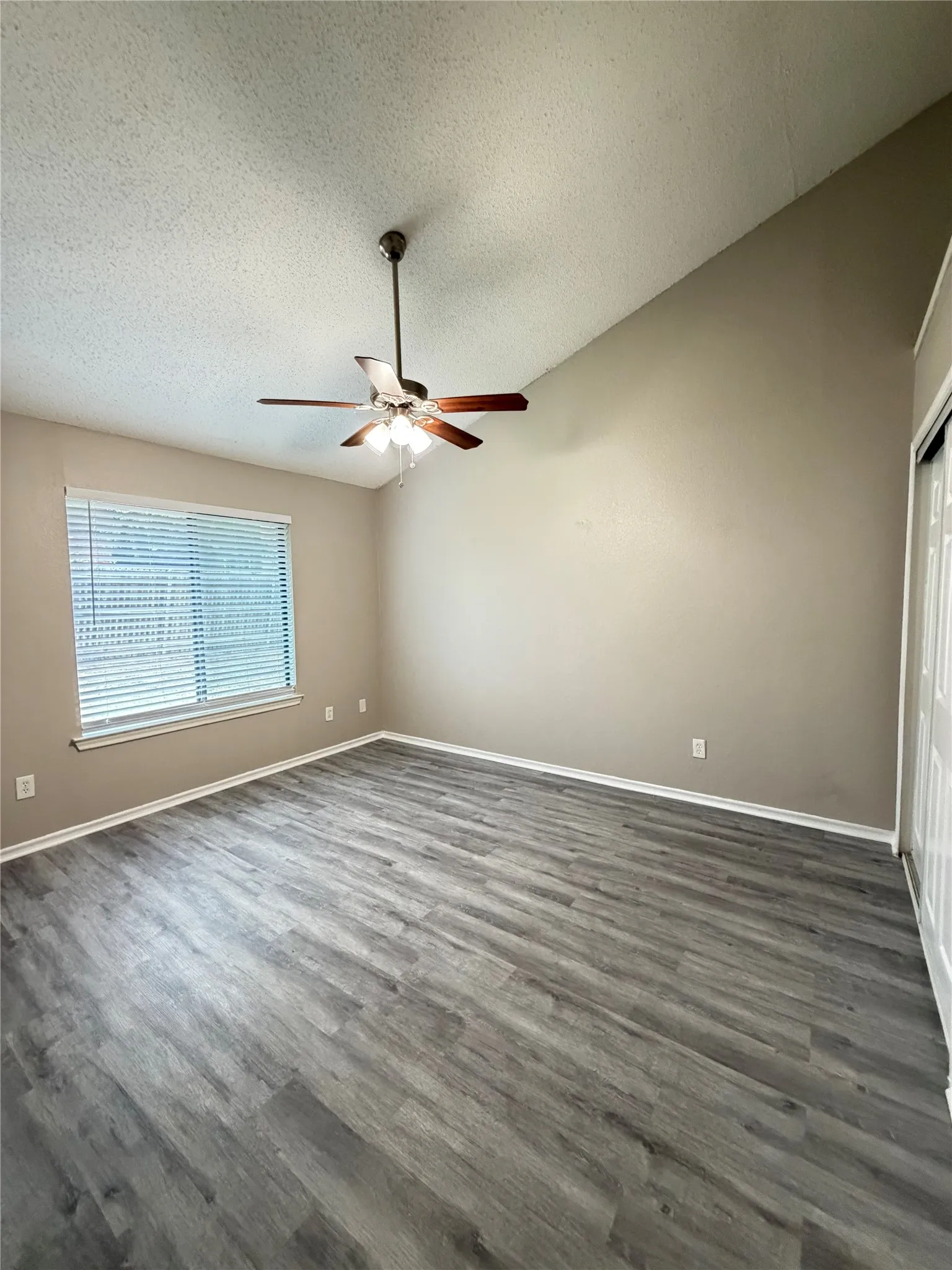 Vaulted ceiling with wood-finish ceiling fan, wood-finish flooring, and window with blinds