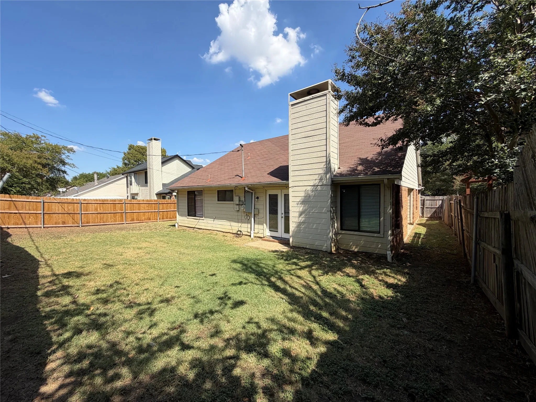 Spacious backyard featuring a wood privacy fence, mature trees, and a ground-level patio