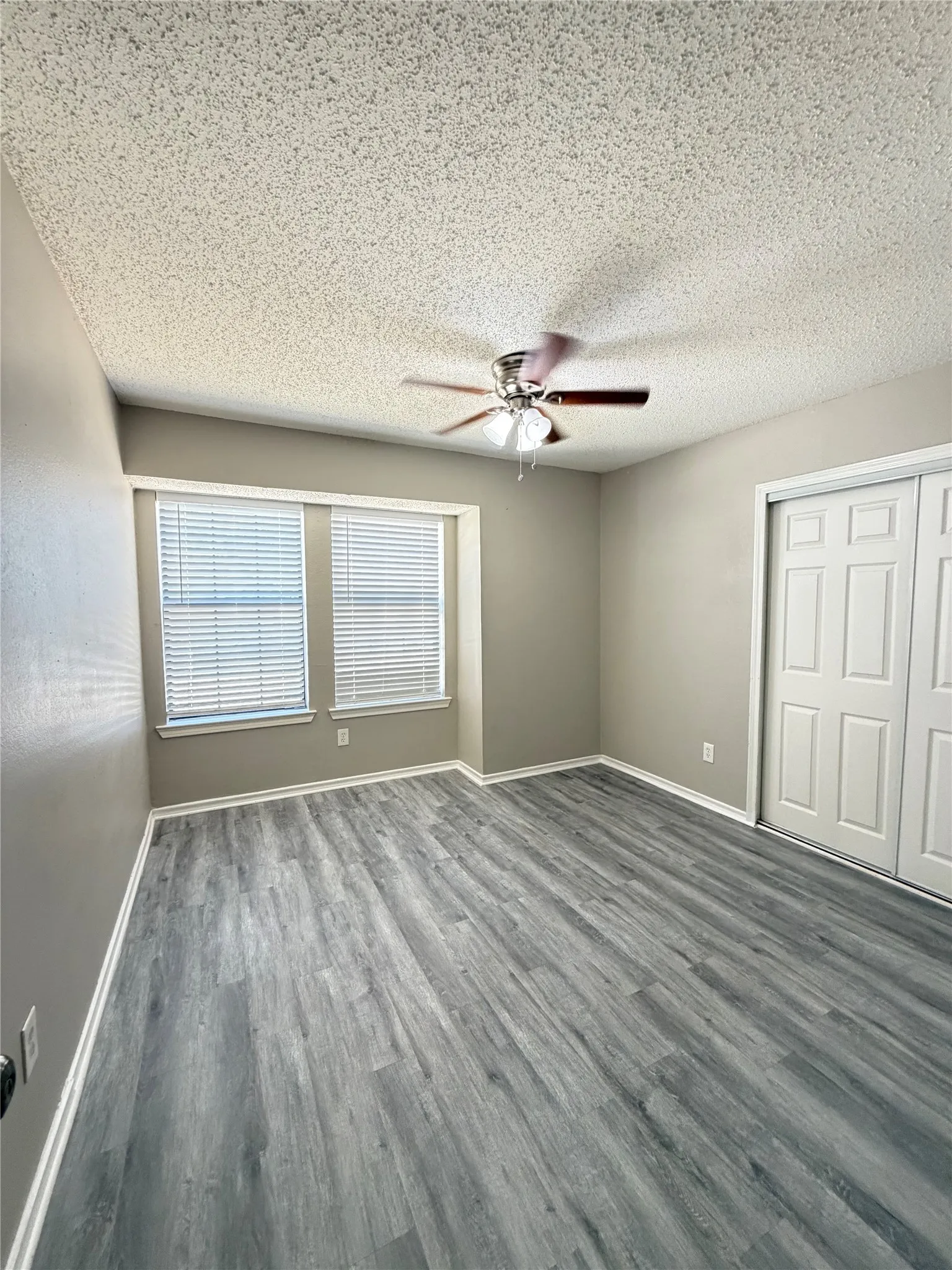 Wood-finish flooring, dual windows with blinds, ceiling fan with light fixture, and bifold closet doors