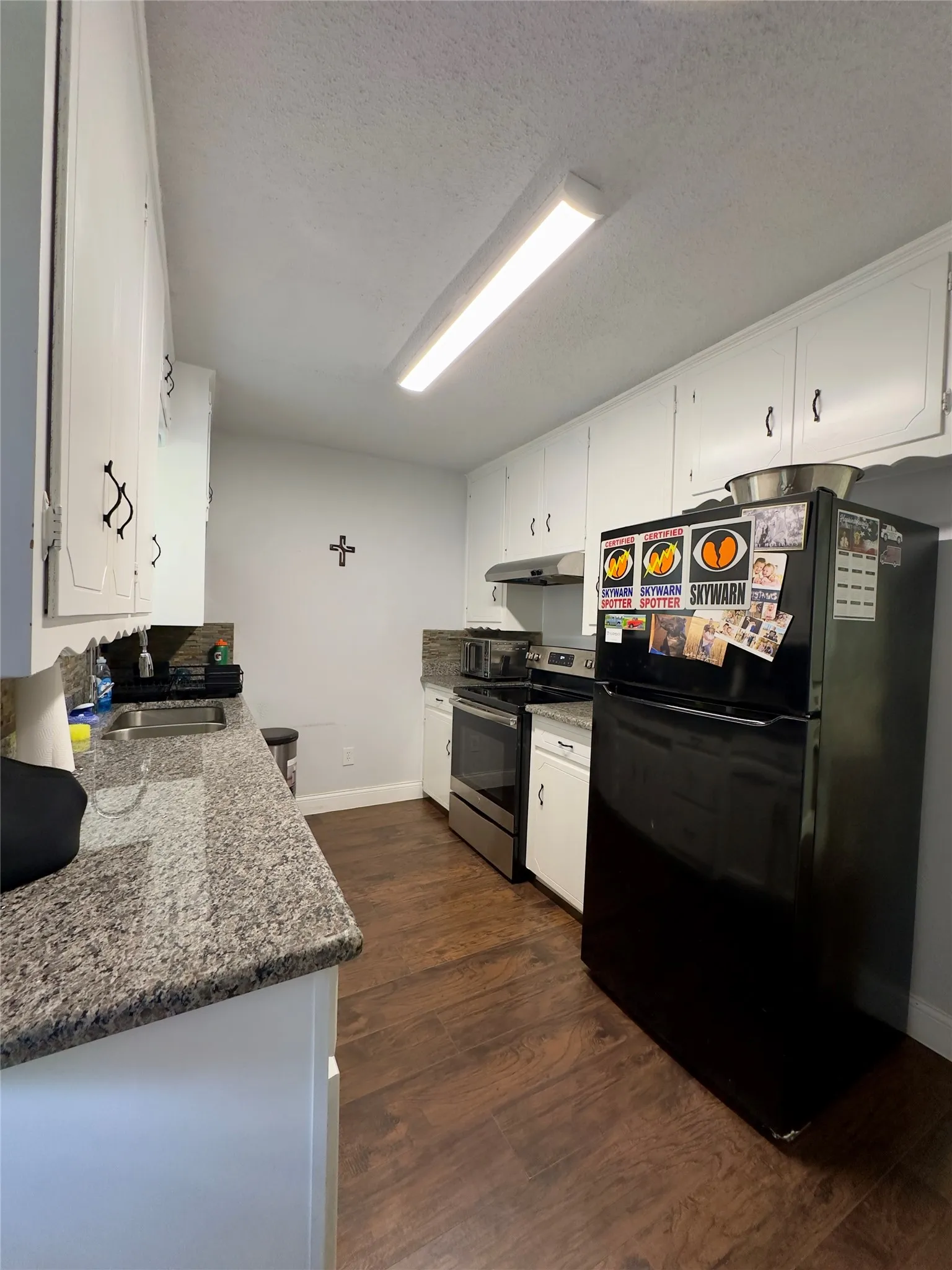 Kitchen featuring wood-finish flooring, white cabinetry with dark hardware, granite-style countertops, and a subway tile backsplash