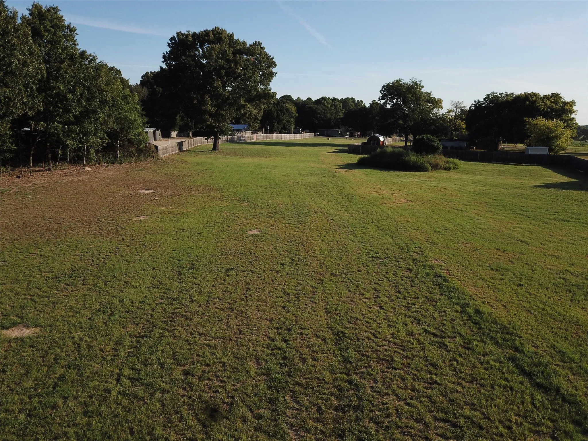 Expansive grass field with perimeter fencing, mature trees, and natural landscaping