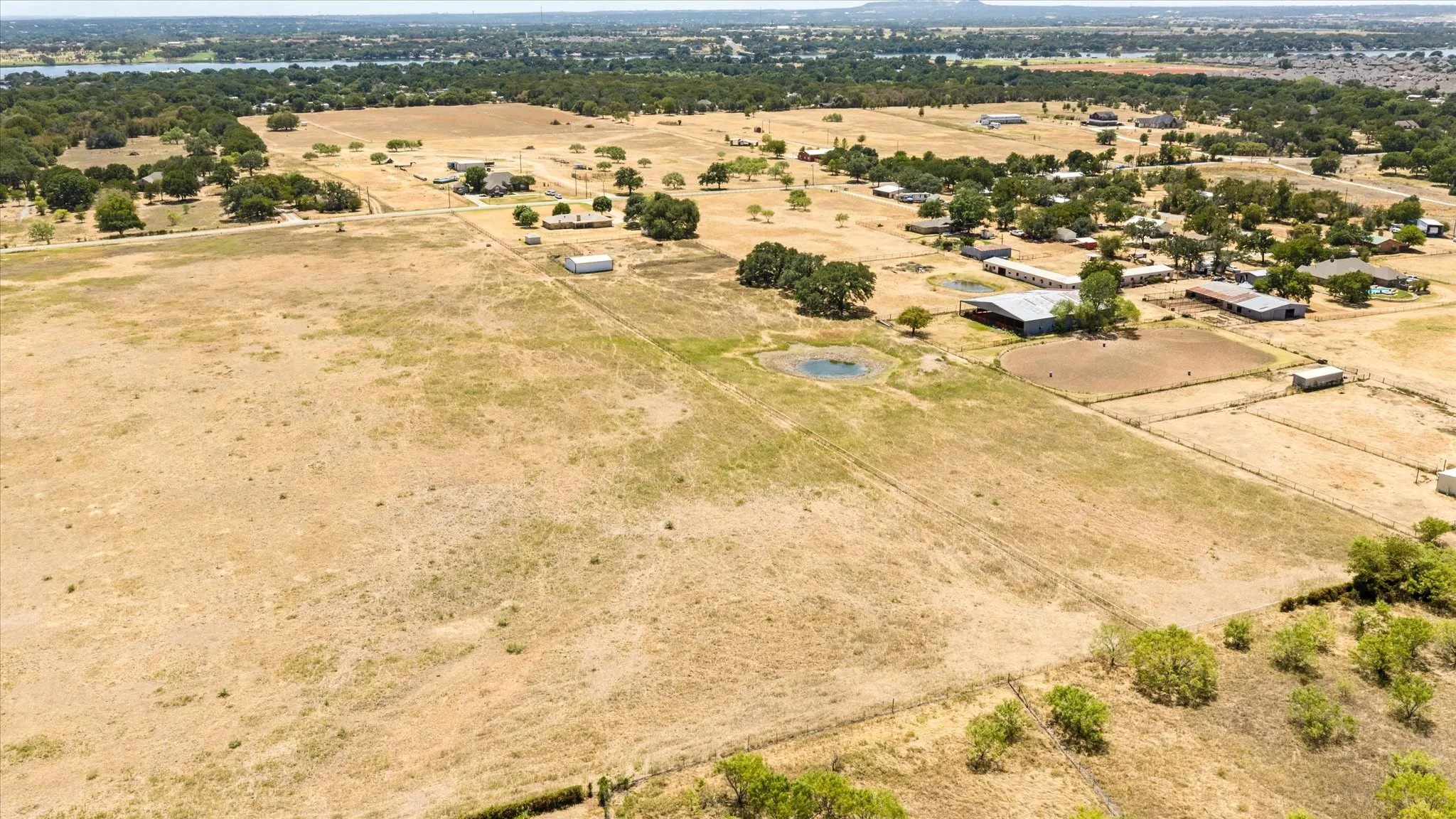 Expansive rural property featuring a natural pond, multiple outbuildings, and mature trees, surrounded by open fields