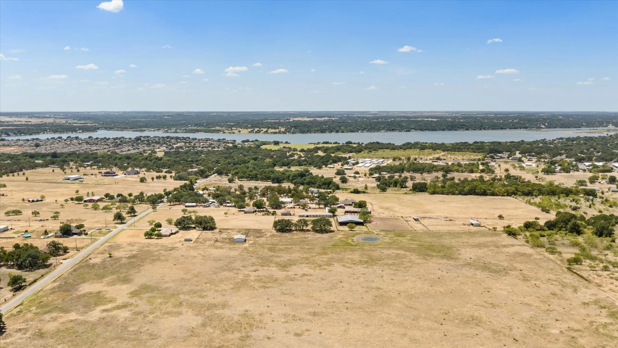 Expansive land parcel featuring a visible road, scattered mature trees, and distant lake
