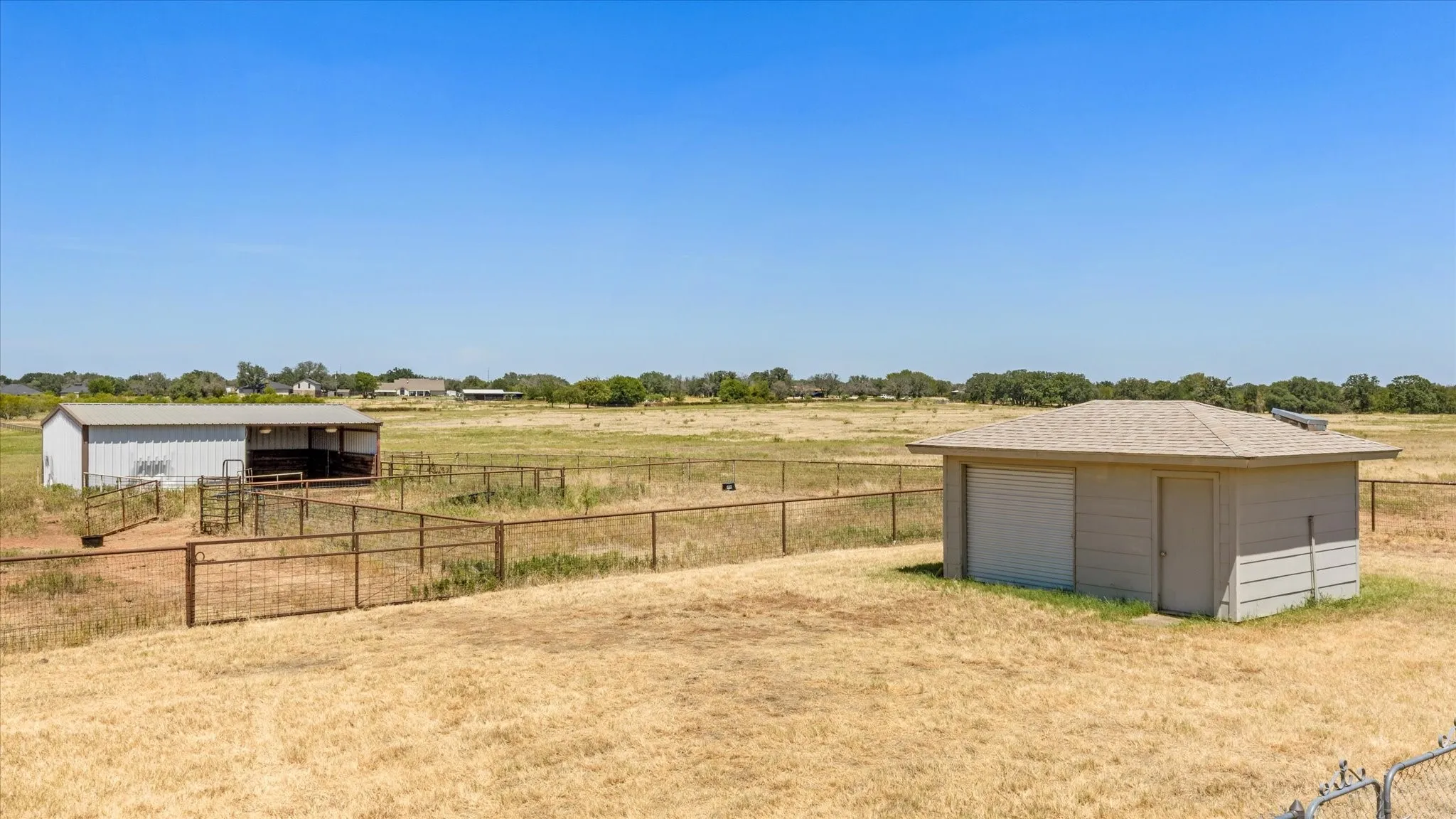 Expansive land with multiple outbuildings, including a metal-sided barn, fenced enclosures, and an additional storage building with garage doors