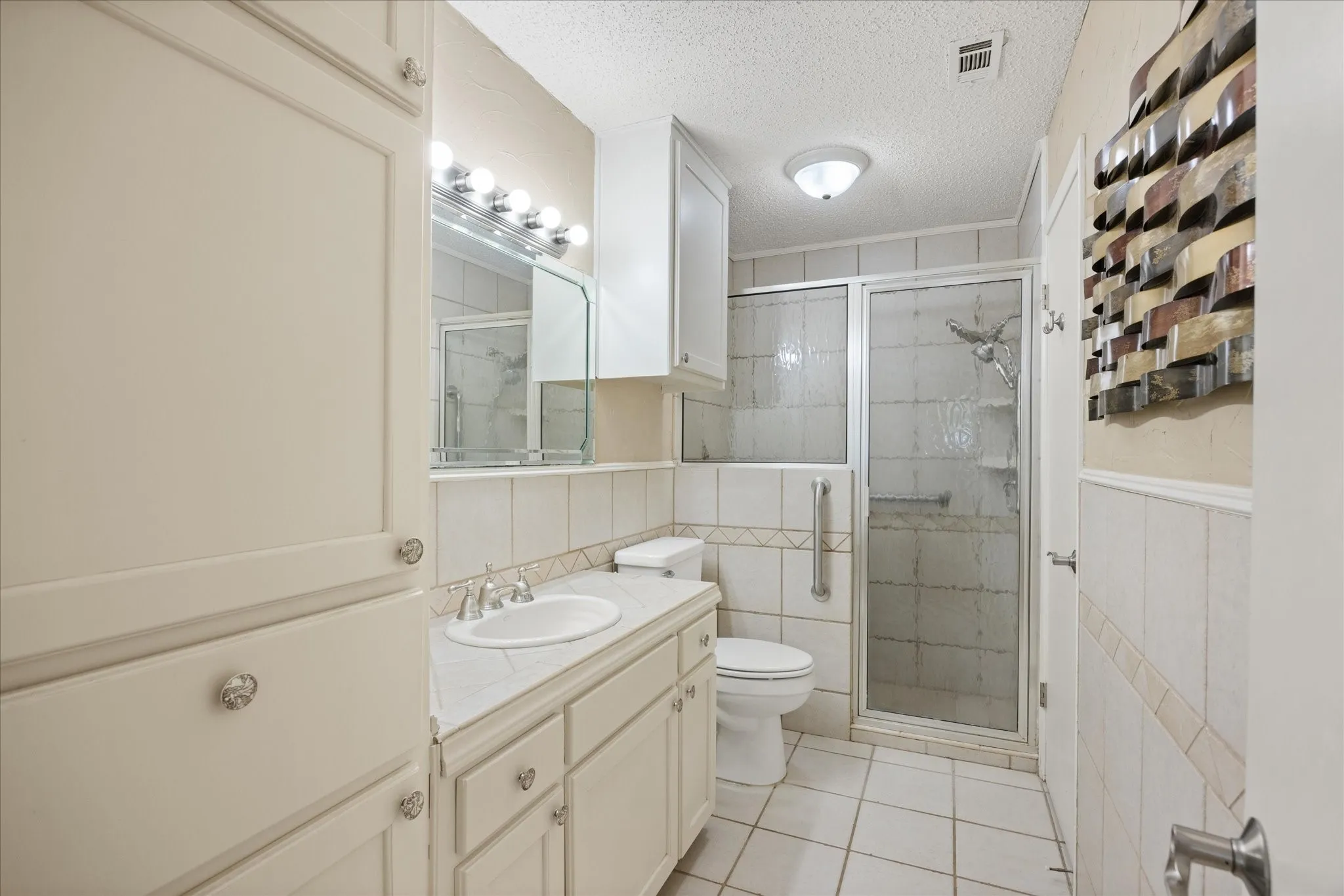 Vanity with integrated sink, extensive built-in cabinetry, tiled shower with glass enclosure, toilet, and flush-mount ceiling light