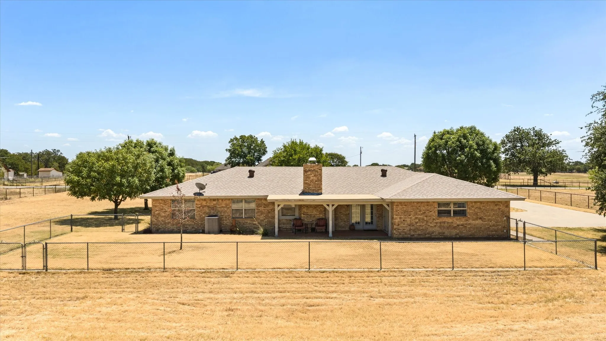 Brick exterior, covered patio, shingle roof, chimney, chain link fencing
