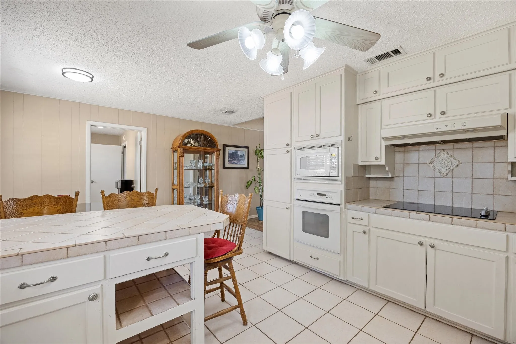 Kitchen featuring white cabinetry, tile countertops, built-in microwave and oven, an electric cooktop, and a ceiling fan with integrated lighting