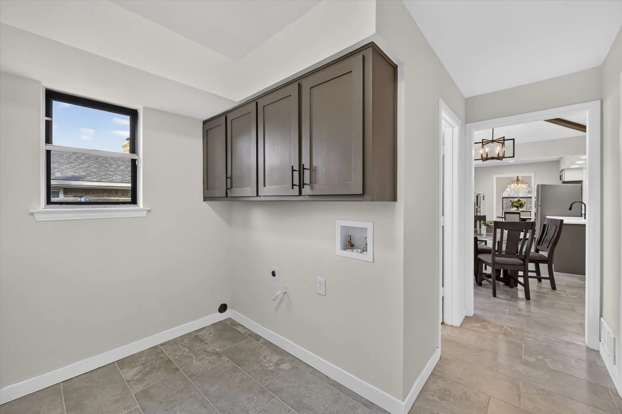 Laundry area featuring upper cabinetry, tile flooring, and a window with black trim