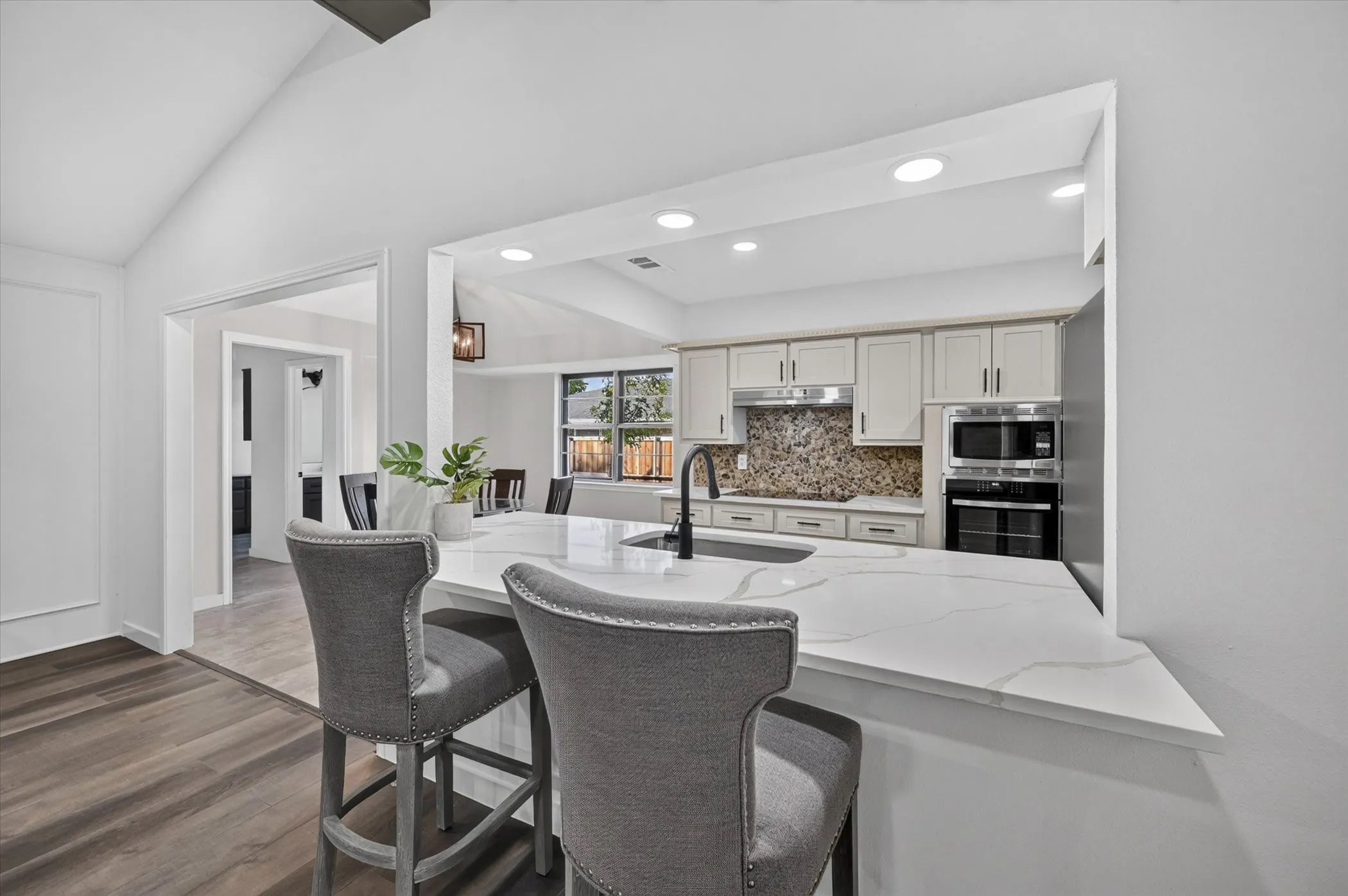 Kitchen featuring an eat-at island with a white countertop, light-colored cabinetry, a mosaic tile backsplash, and stainless-steel appliances