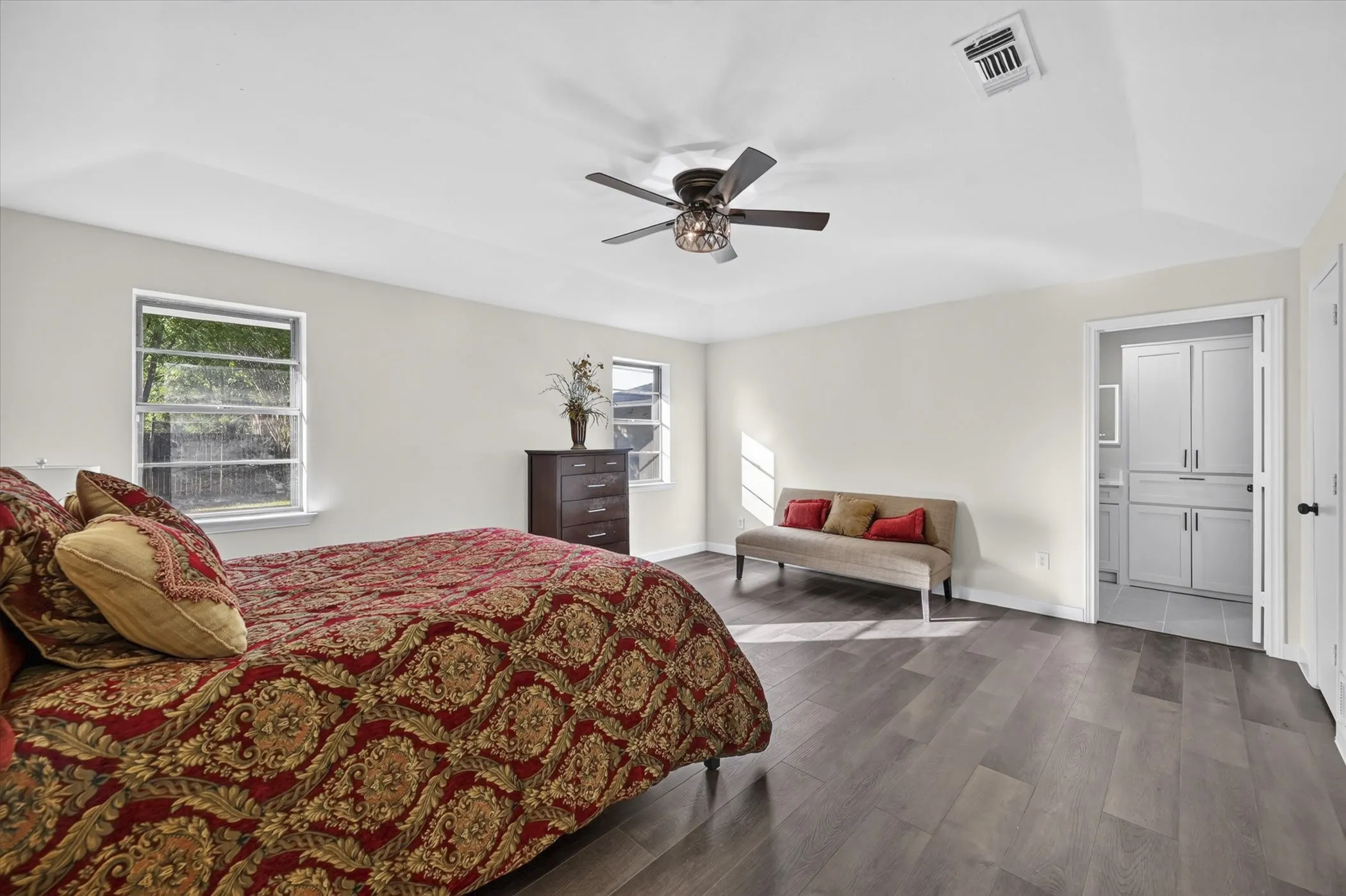 Wood-finish flooring throughout, ceiling fan with integrated lighting, two windows, and an en-suite entrance featuring built-in cabinetry